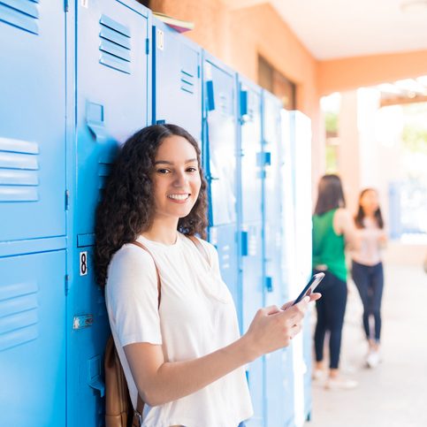 Smiling Caucasian teenager using smartphone in high school corridor